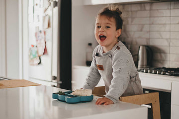 Toddler eating meal at kitchen bench